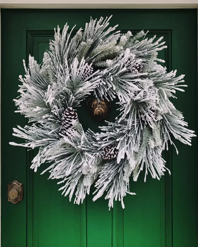 A frosted winter wreath on a green front door with brass hardware